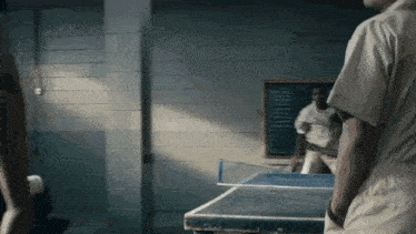 a man is playing ping pong with another man