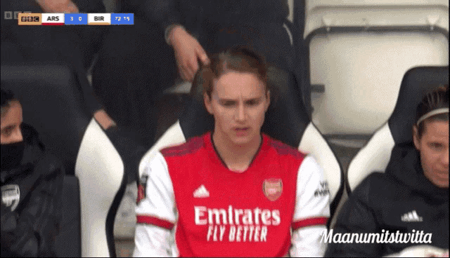 a man wearing an emirates fly better shirt sits in a stadium