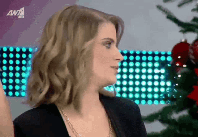 a woman is standing in front of a christmas tree and a sign that says ant 1