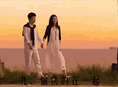a man and a woman are holding hands while walking in front of the ocean at sunset .