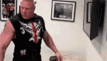 a man in a wrestling shirt is standing in a room holding a can of popcorn .