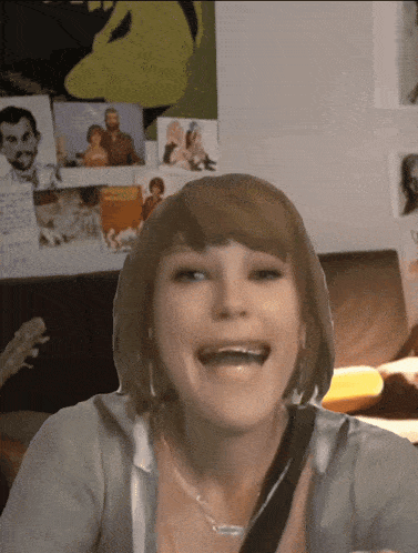 a woman is laughing in front of a wall with posters on it