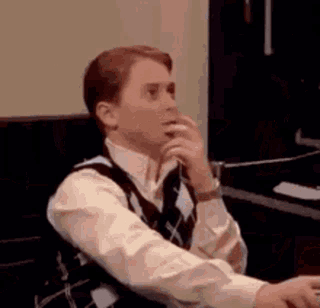 a man is sitting at a desk with his hand on his chin and looking at something .