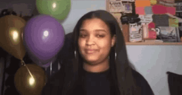a woman is standing in front of balloons and making a funny face .