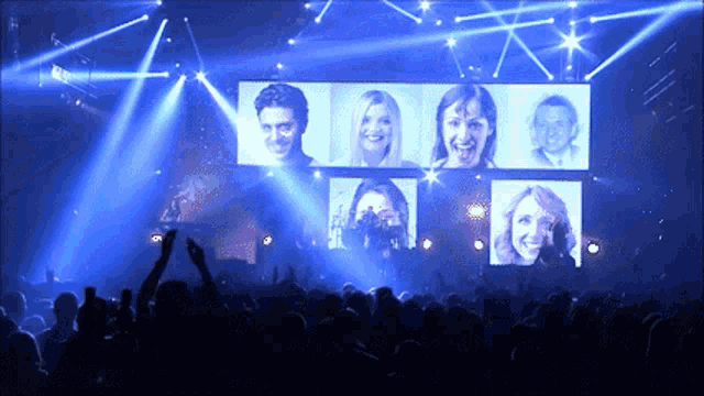 a crowd of people watching a concert with a large screen showing a man and three women