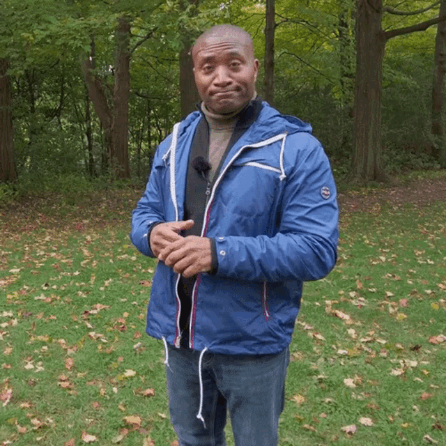 a man in a blue jacket stands in a field with trees in the background