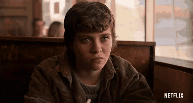 a young girl is sitting at a table in a diner and looking at the camera .