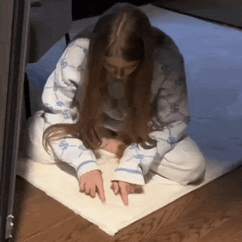 a woman in pajamas is sitting on the floor pointing at something