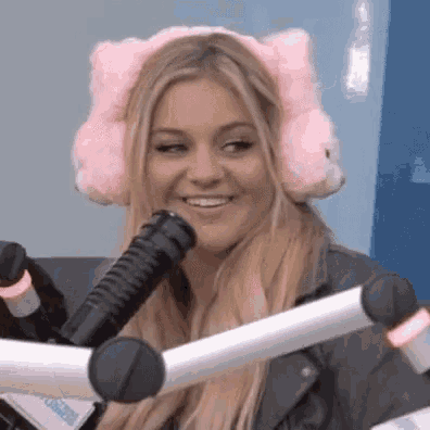 a woman wearing a pink cat ear muff is smiling in front of a microphone .