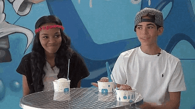 a boy and a girl are sitting at a table with ice cream cups on it