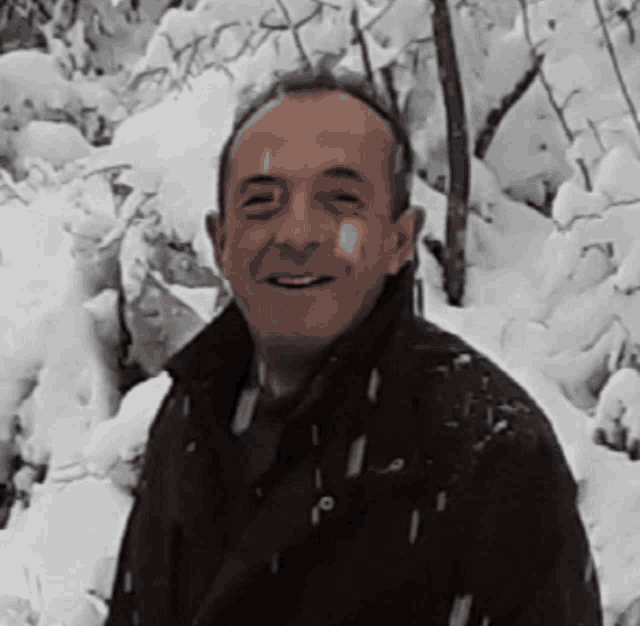 a man in a brown jacket is smiling in front of a snowy forest