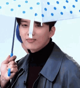 a man in a blue jacket is holding an umbrella with blue polka dots on it .