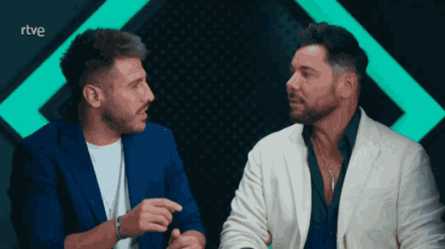 two men are sitting next to each other in front of a green light and the word rtve is on the bottom right