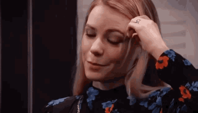 a woman in a floral top is touching her forehead .