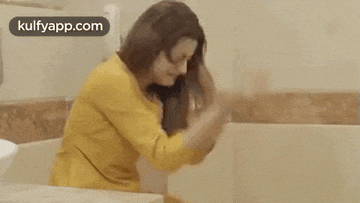 a woman in a yellow dress is sitting in a bathtub and washing her hair .