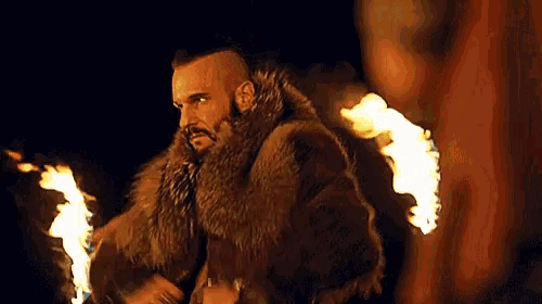 a man in a fur coat is standing next to a fire .