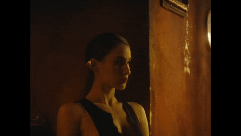 a woman in a black dress stands in front of a wooden wall