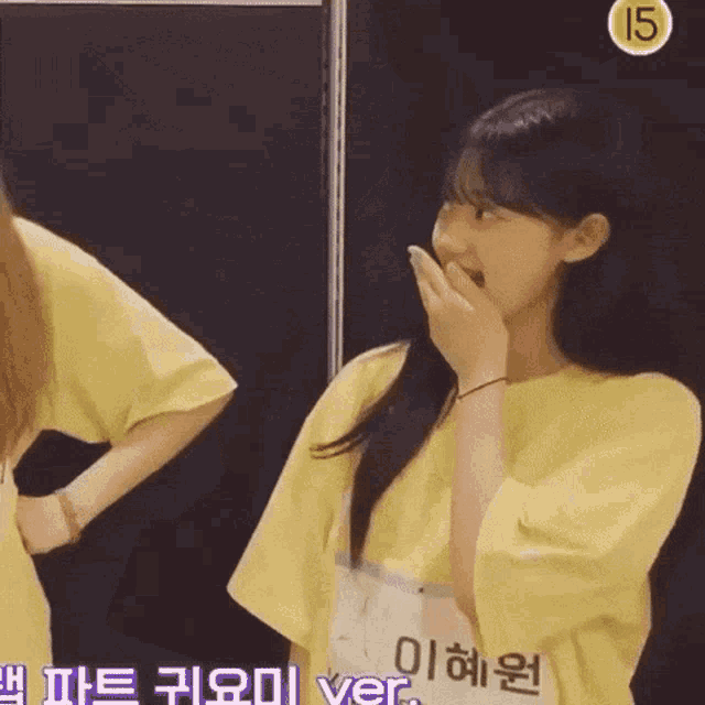 two girls are standing next to each other and one has a yellow shirt on with the number 15 on it .