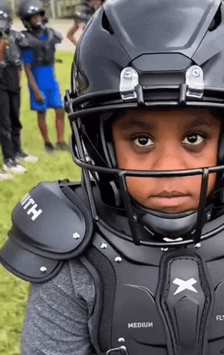 a young boy wearing a football helmet and shoulder pads with the word medium on the chest