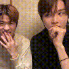 two young men are sitting next to each other and one of them is covering his mouth with his hand .