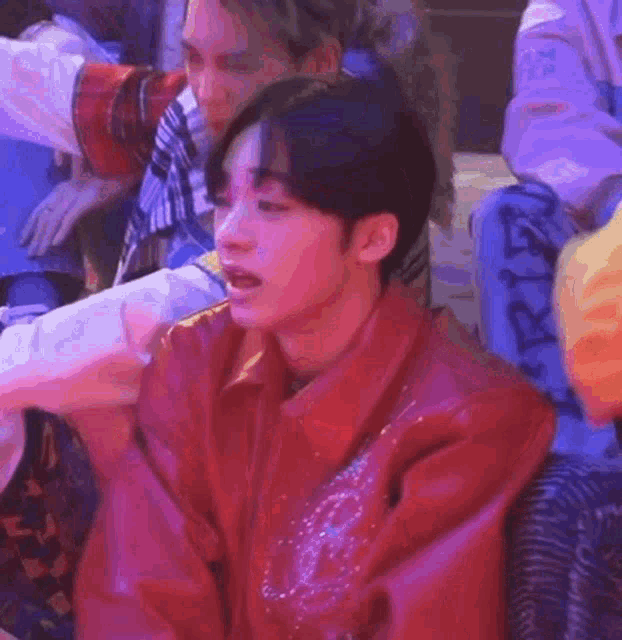 a man in a red jacket is sitting in a chair in a room with other people .