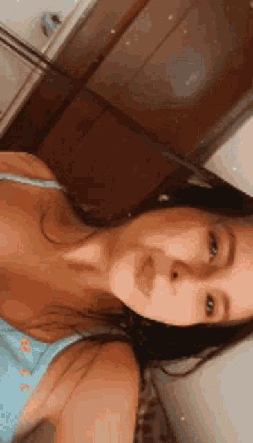 a woman in a blue tank top is taking a selfie in a room .
