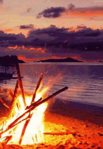 a campfire on a beach with a boat in the background