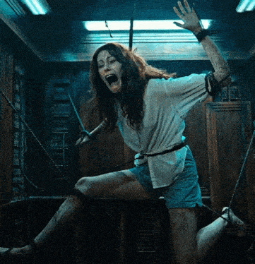 a woman in a white shirt and blue shorts is chained up and screaming