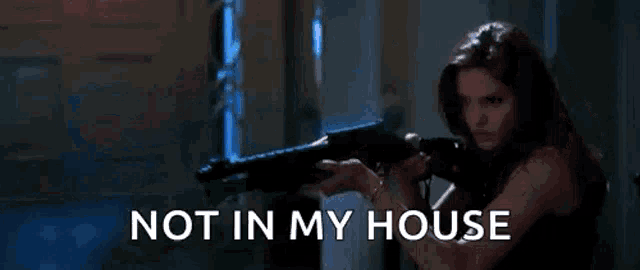 a woman is holding a gun with the words not in my house written below her .