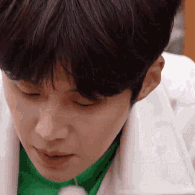 a close up of a young man wearing a green shirt and a white jacket .
