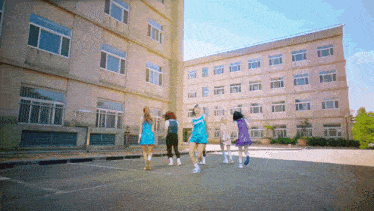 a group of girls are dancing in a parking lot in front of a building