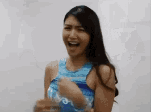 a woman in a blue tank top is laughing while holding a glass of water .