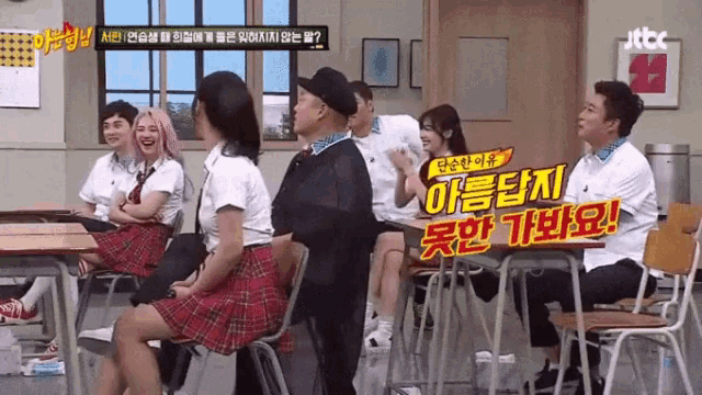a group of people are sitting at desks in a classroom with a sign that says jtbc on it .