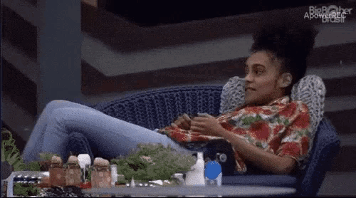 a woman is laying on a couch with a big brother brasil logo on the bottom