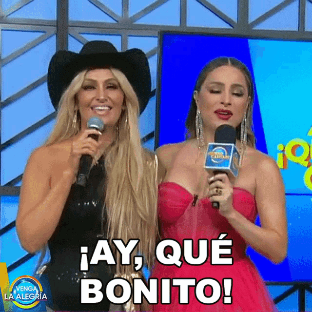 two women are holding microphones and one of them is saying " ay que bonito "