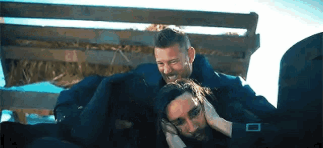 two men are sitting next to each other on a bench and one of them is holding the other 's head .