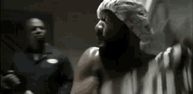 a man with a beard is wearing a shower cap while another man looks on .