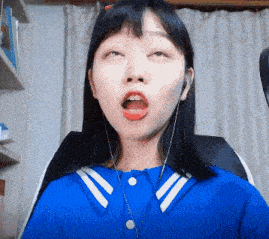a woman wearing headphones and a blue shirt is making a funny face while sitting in a chair .
