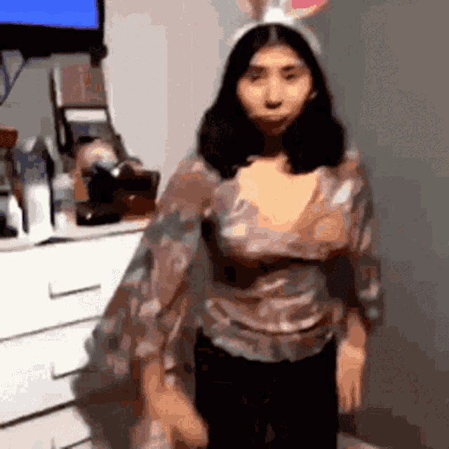 a woman wearing bunny ears and a floral shirt is standing in front of a dresser .