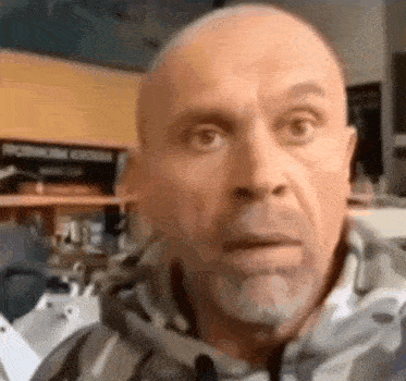 a bald man with a beard is making a funny face while wearing a hoodie .