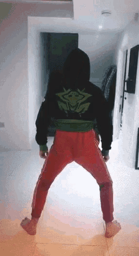 a person in a black hoodie and red pants is standing on their feet in a hallway .