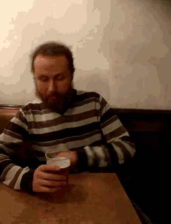 a man with a beard sits at a table with a glass of beer