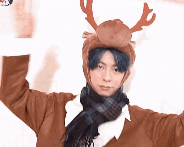 a man with blue hair wears a reindeer hat and scarf
