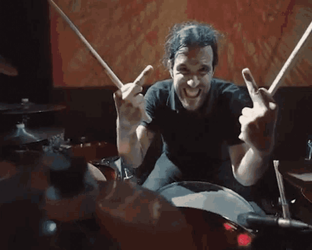 a man in a black shirt is playing the drums and giving the middle finger