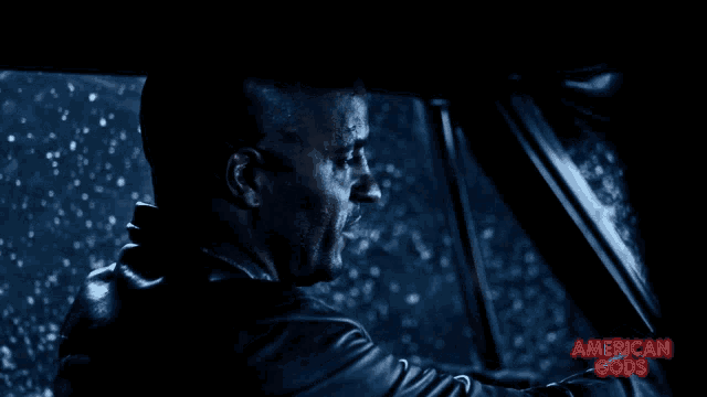 a man driving a car with the words american gods written on the bottom