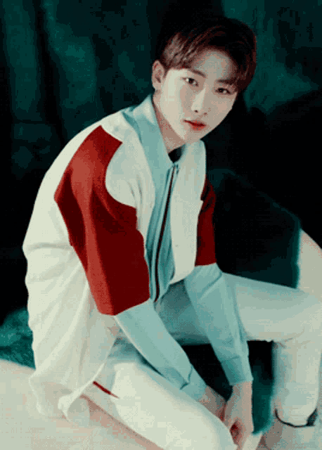 a young man wearing a red white and blue shirt sits on the ground