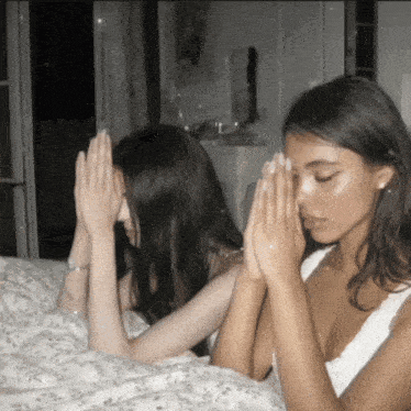 two women praying with their hands folded over their faces