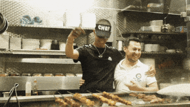 a man in a chef hat stands next to another man in a white shirt