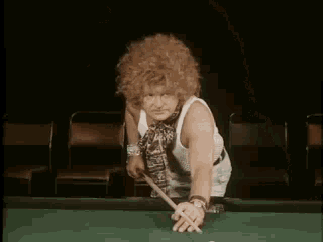 a man with curly red hair and a scarf around his neck is wearing a white tank top .
