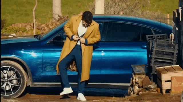 a man in a yellow coat standing next to a blue car
